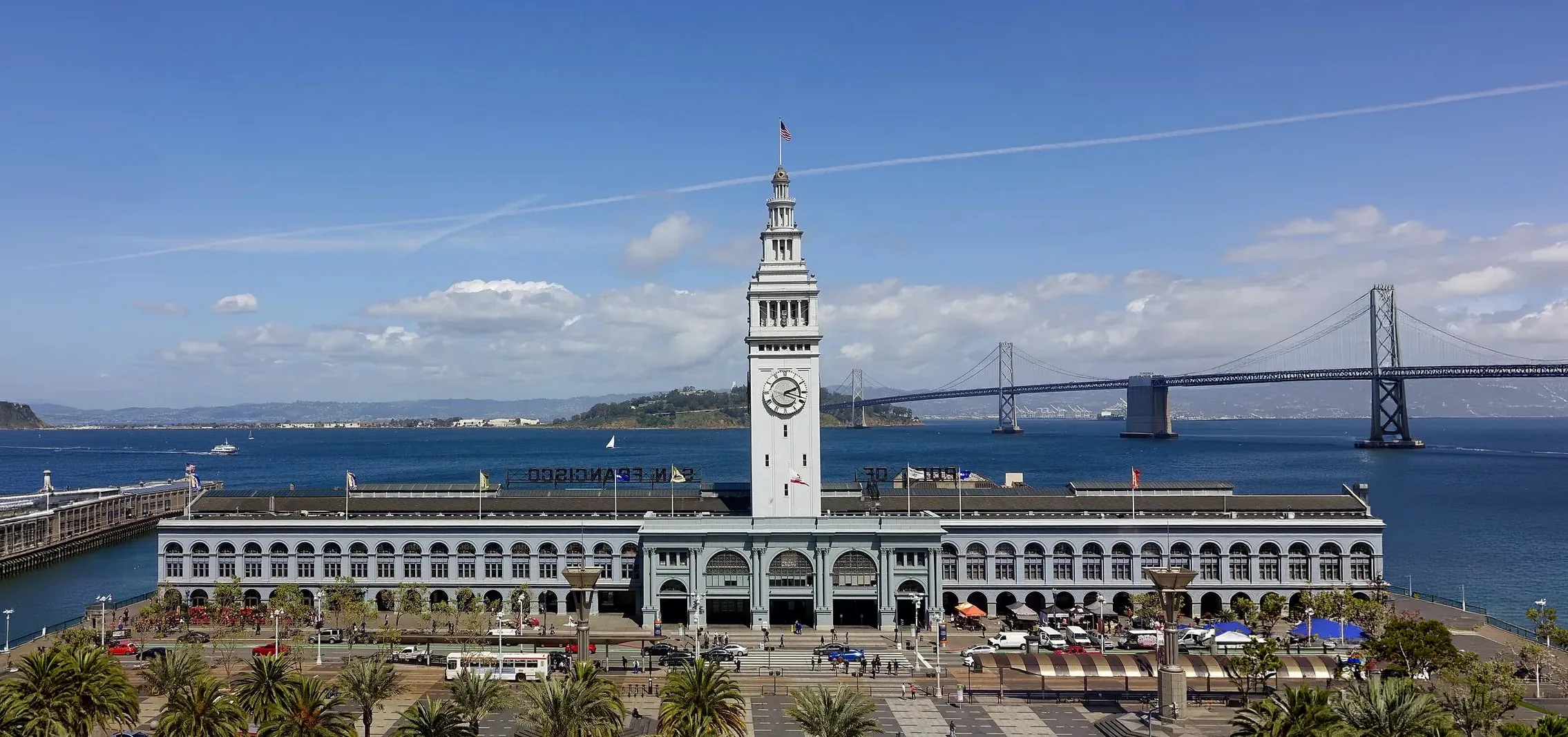 The front of the San Francisco Ferry Building and its clock tower, with the Bay Bridge behind it