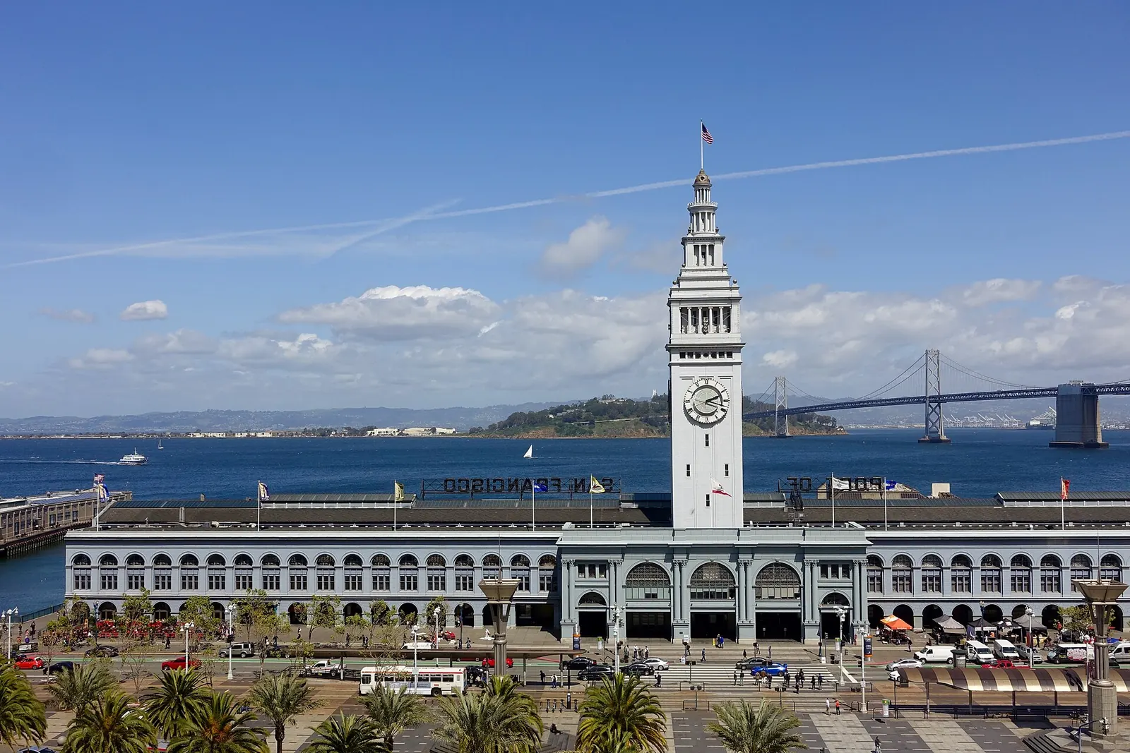 The front of the San Francisco Ferry Building and its clock tower, with the Bay Bridge behind it