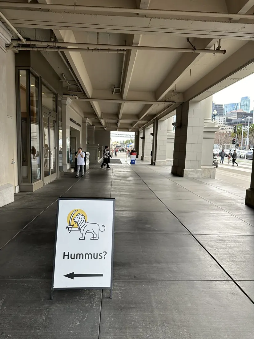 An Obour sign with the lion logo reading Hummus? and an arrow, under the Ferry Building arcade
