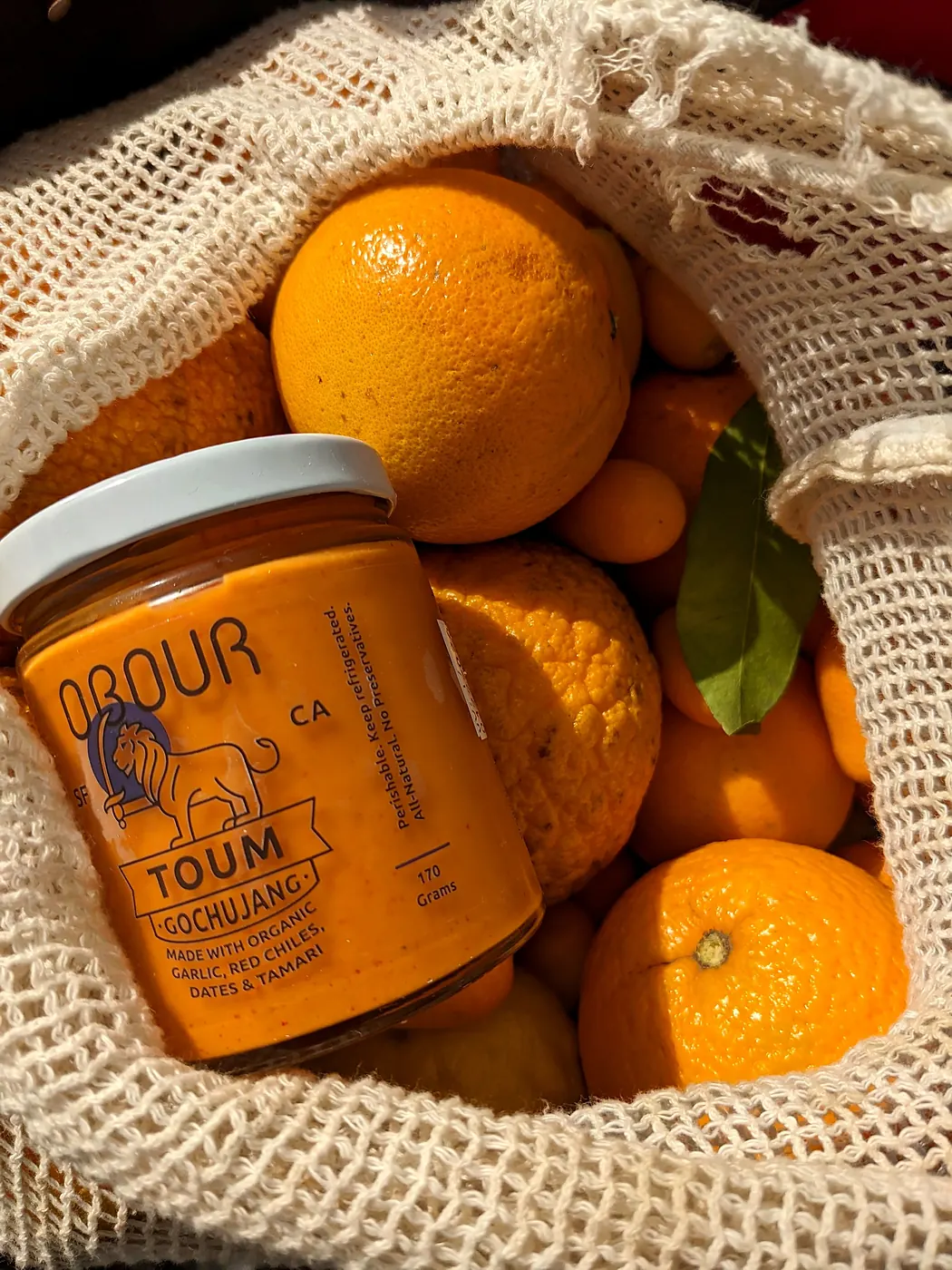 A jar of Obour Gochujang toum in a mesh bag full of oranges