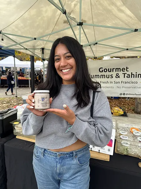 A smiling shopper holding a jar of Obour hummus at the stand