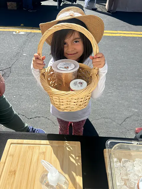 A child in a sun hat holding up a basket with a tub of Obour hummus
