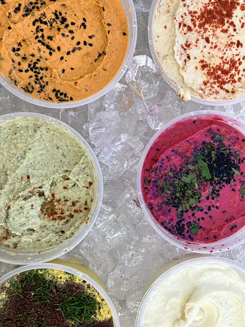 Tubs of Berbere, Classic, Zhoug and Red Beet hummus on ice, seen from above