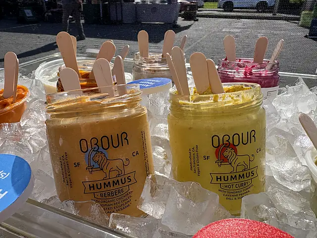 Jars of Obour Berbere and Hot Curry hummus on ice, with tasting spoons behind them