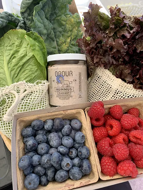 A jar of Obour Black Bean hummus among lettuces, blueberries and raspberries