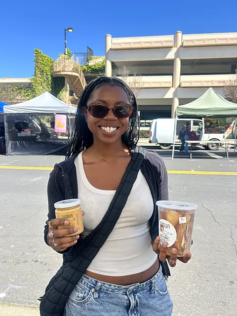 A smiling shopper holding a jar of hummus and a tub of pita chips