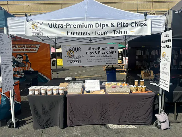 The Obour tent with an Ultra-Premium Dips & Pita Chips banner and a table of jars, samples and chips