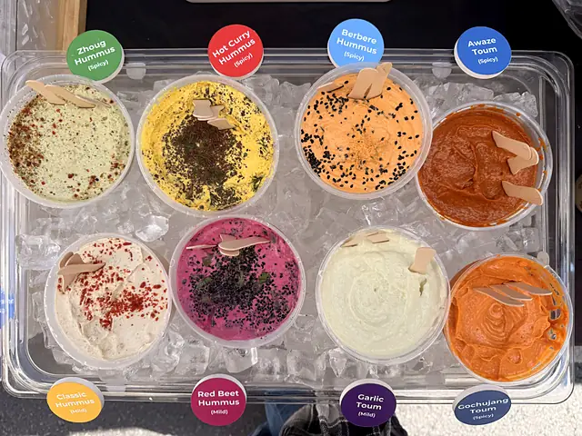 A tray of eight Obour hummus and toum samples on ice with flavor labels