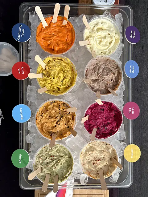 A tray of Obour hummus and toum samples on ice, each labeled with its flavor, seen from above