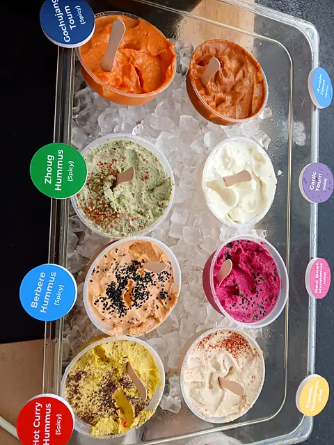 A tray of Obour hummus and toum samples on ice with round flavor labels