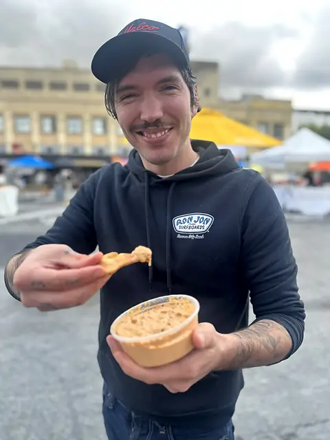 A smiling shopper dipping a pita chip into a tub of Obour hummus