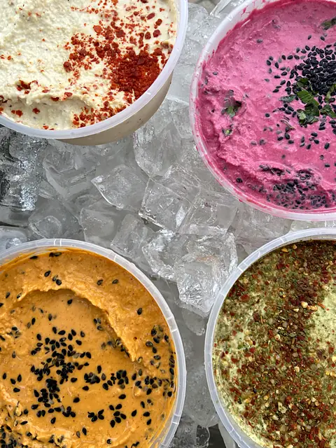Tubs of Classic, Red Beet, Berbere and Zhoug hummus on ice, seen from above