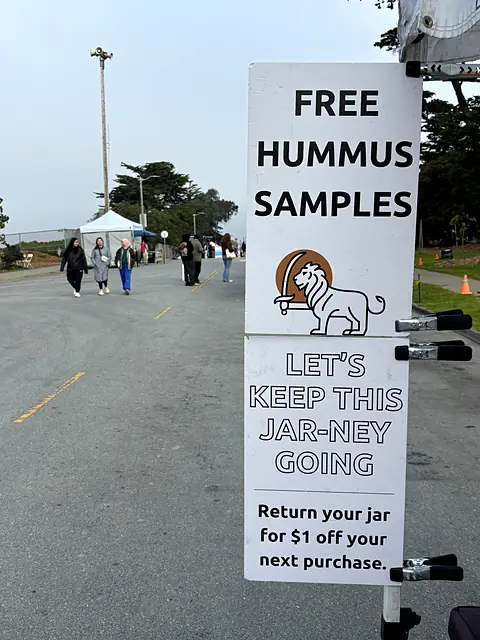 The Obour free hummus samples sign at the edge of a market