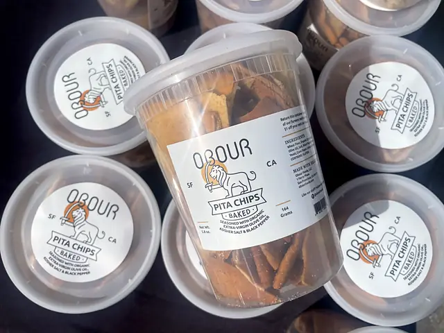 A tub of Obour pita chips held above a table of more tubs
