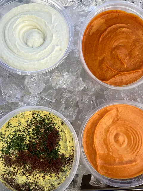 Tubs of Garlic toum, Gochujang toum and Hot Curry hummus on ice, seen from above