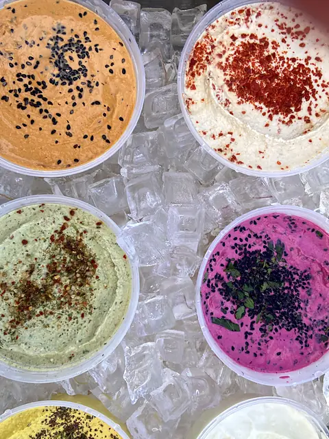 Four garnished tubs of Obour hummus on ice, seen from above