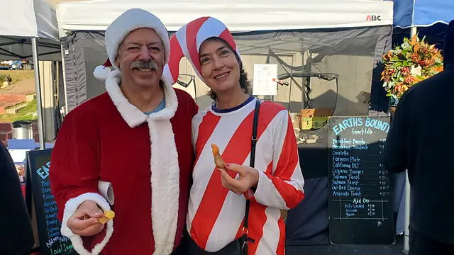 Two market-goers in Santa and candy-cane costumes holding up samples