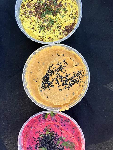 Tubs of Hot Curry, Berbere and Red Beet hummus in a row, seen from above
