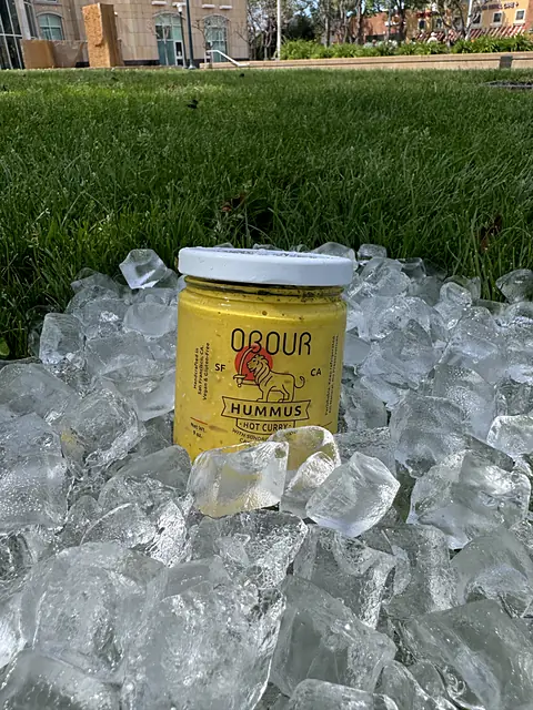 A jar of Obour Hot Curry hummus in a pile of ice on the grass