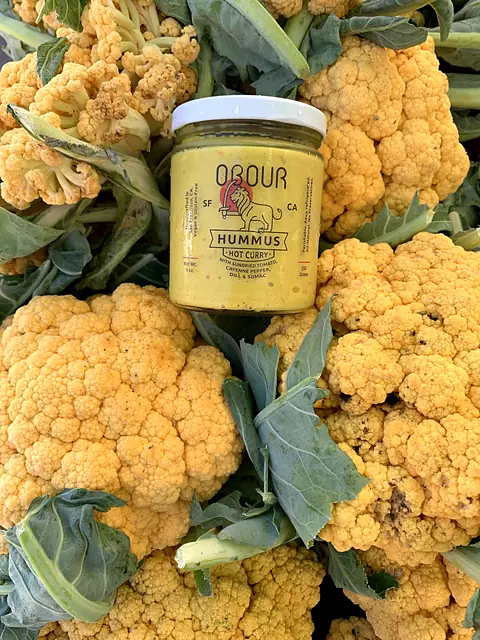 A jar of Obour Hot Curry hummus resting on a pile of orange cauliflower