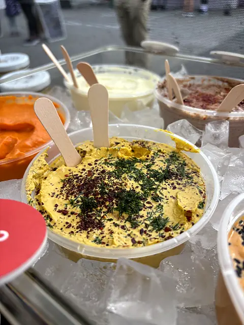 A tub of Obour Hot Curry hummus with wooden tasting spoons