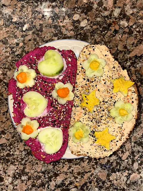 Red Beet and Classic hummus spread on flatbread and decorated with cucumber flowers and stars