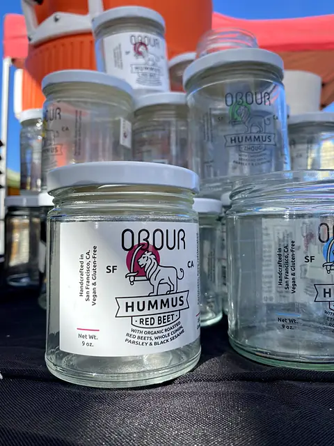 Empty Obour glass jars stacked at a market stand, an empty Red Beet hummus jar in front