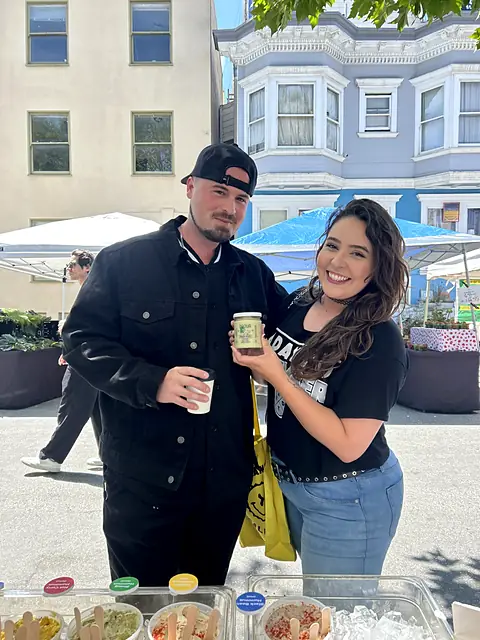 A couple holding a jar of Obour Zhoug hummus at the stand