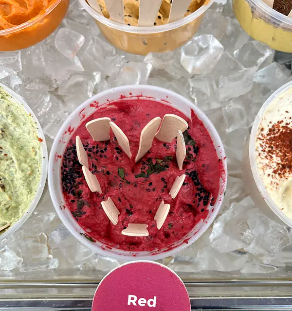A tub of Obour Red Beet hummus on ice with tasting spoons arranged in a heart