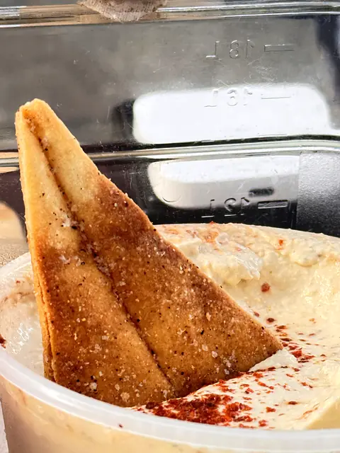 A pita chip standing in a tub of Obour Classic hummus dusted with chile
