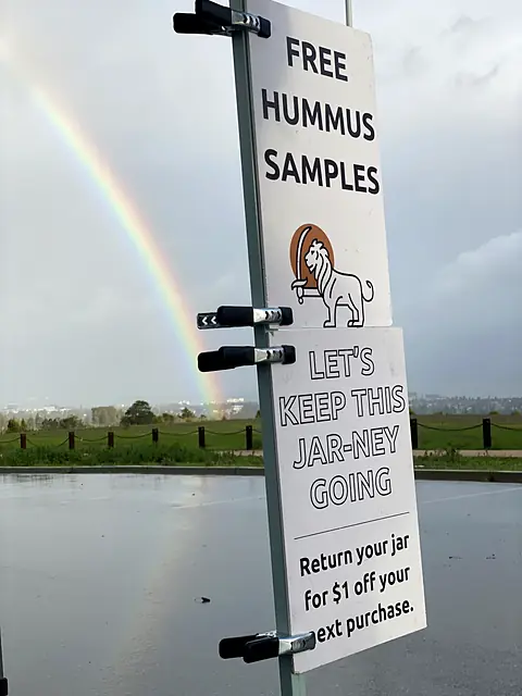 The Obour free hummus samples sign on a rainy morning, with a rainbow behind it