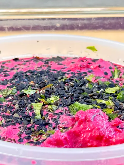 A close-up of Obour Red Beet hummus topped with black sesame and chopped herbs