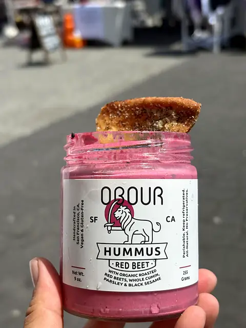 A jar of Obour Red Beet hummus with a pita chip resting on top