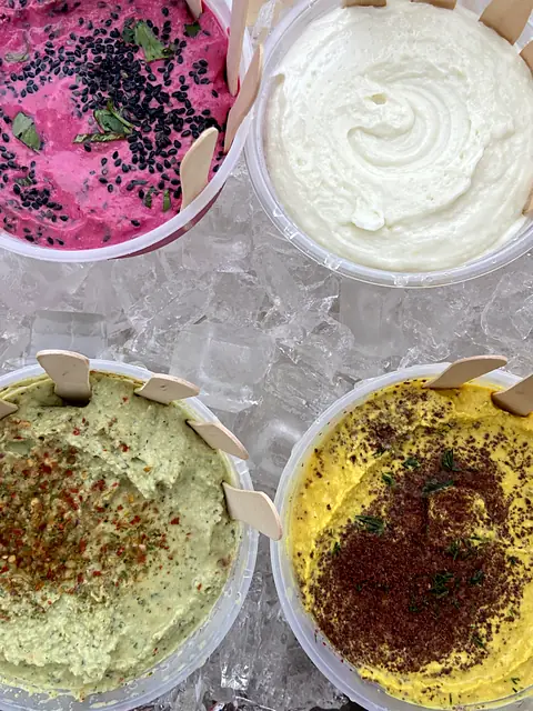 Tubs of Red Beet hummus, Garlic toum, Zhoug and Hot Curry on ice, with tasting spoons