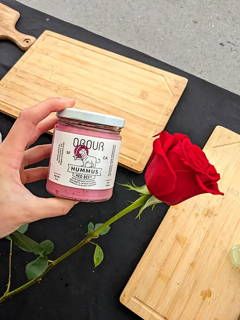 A jar of Obour Red Beet hummus held next to a single red rose on a cutting board