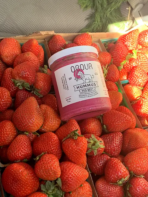 A jar of Obour Red Beet hummus set into a flat of strawberries
