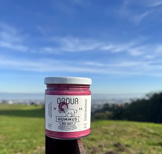 A jar of Obour Red Beet hummus on a post with the bay in the distance