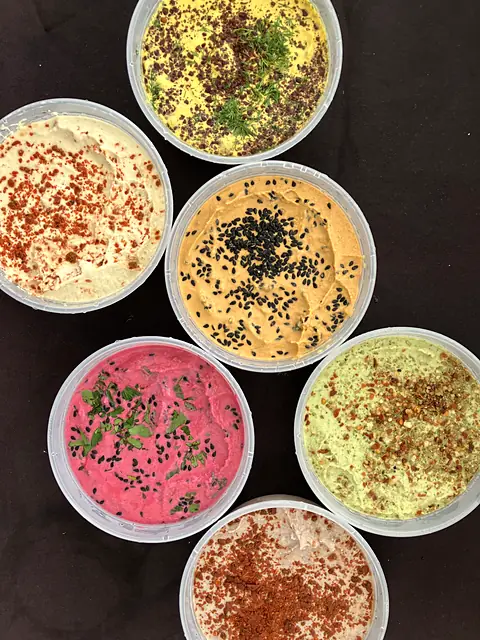 Six garnished tubs of Obour hummus arranged on a black table
