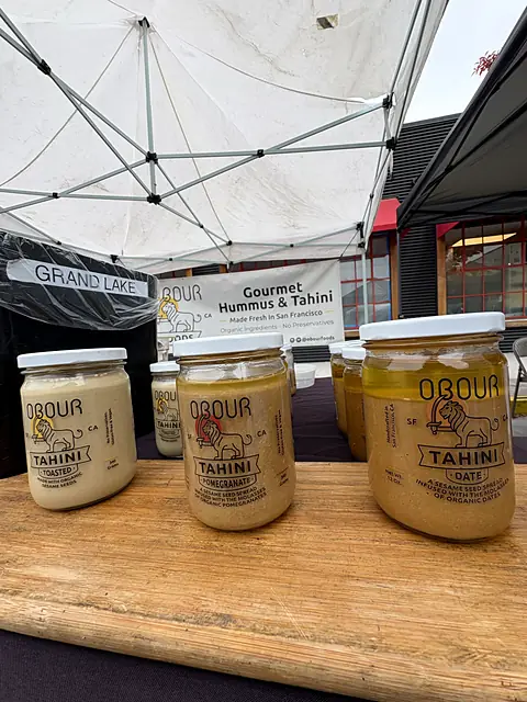 Jars of Obour tahini on a wooden board under the market tent