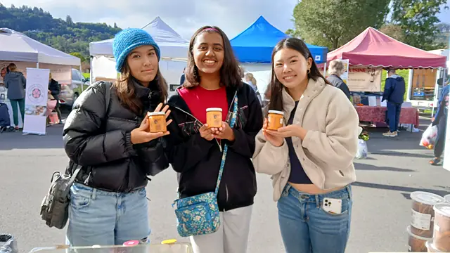 Three friends holding up jars of Obour hummus at a farmers market