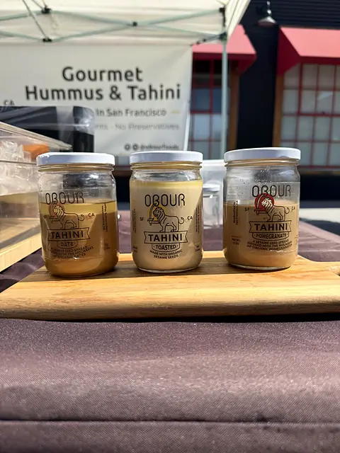 Three jars of Obour tahini on a board in front of the banner