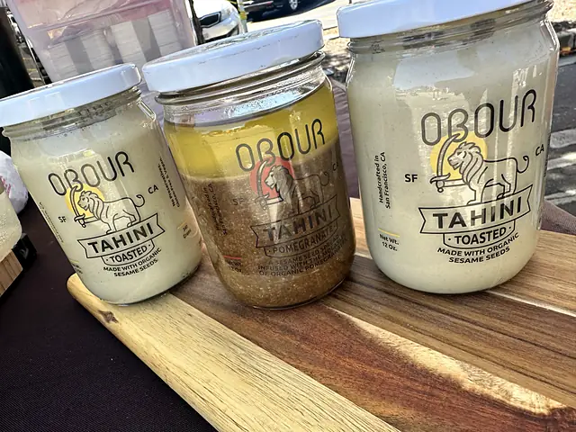 Two jars of Obour Toasted tahini and one of Pomegranate tahini on a wooden board