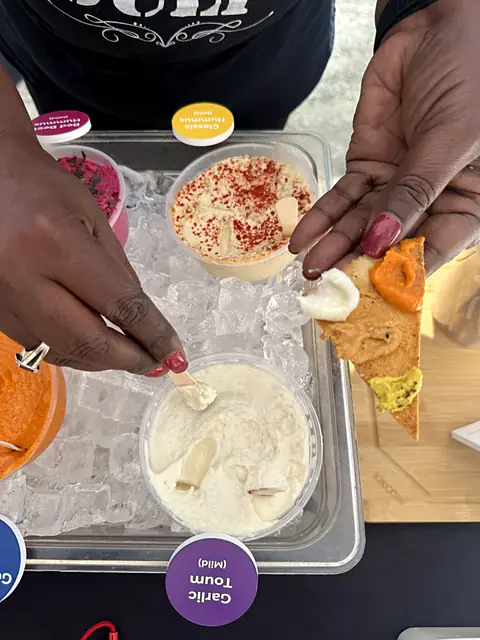 Hands dipping pita chips into sample tubs on ice