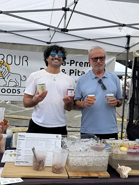 Two people holding jars of Obour hummus under the Obour banner