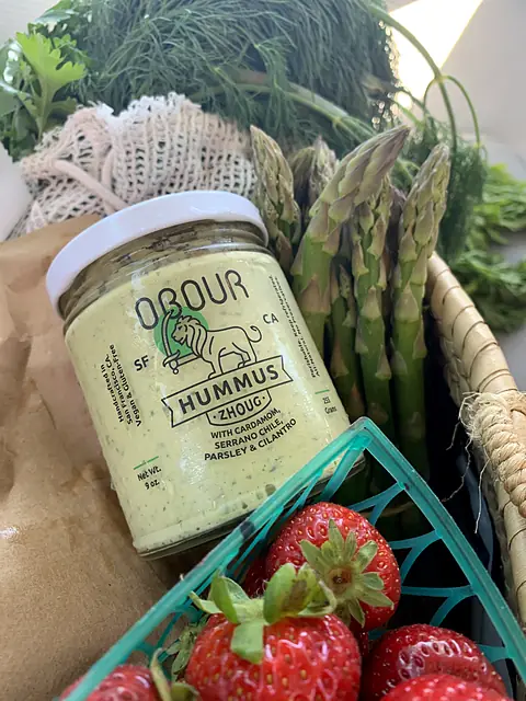A jar of Obour Zhoug hummus with asparagus and a basket of strawberries