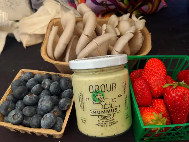 A jar of Obour Zhoug hummus between baskets of blueberries, strawberries and oyster mushrooms