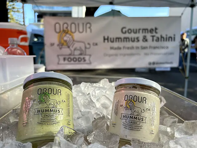 Jars of Obour Zhoug and Classic hummus on ice in front of the Obour banner