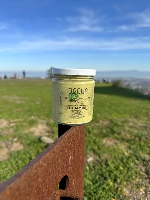 A jar of Obour Zhoug hummus on a post on a grassy hilltop
