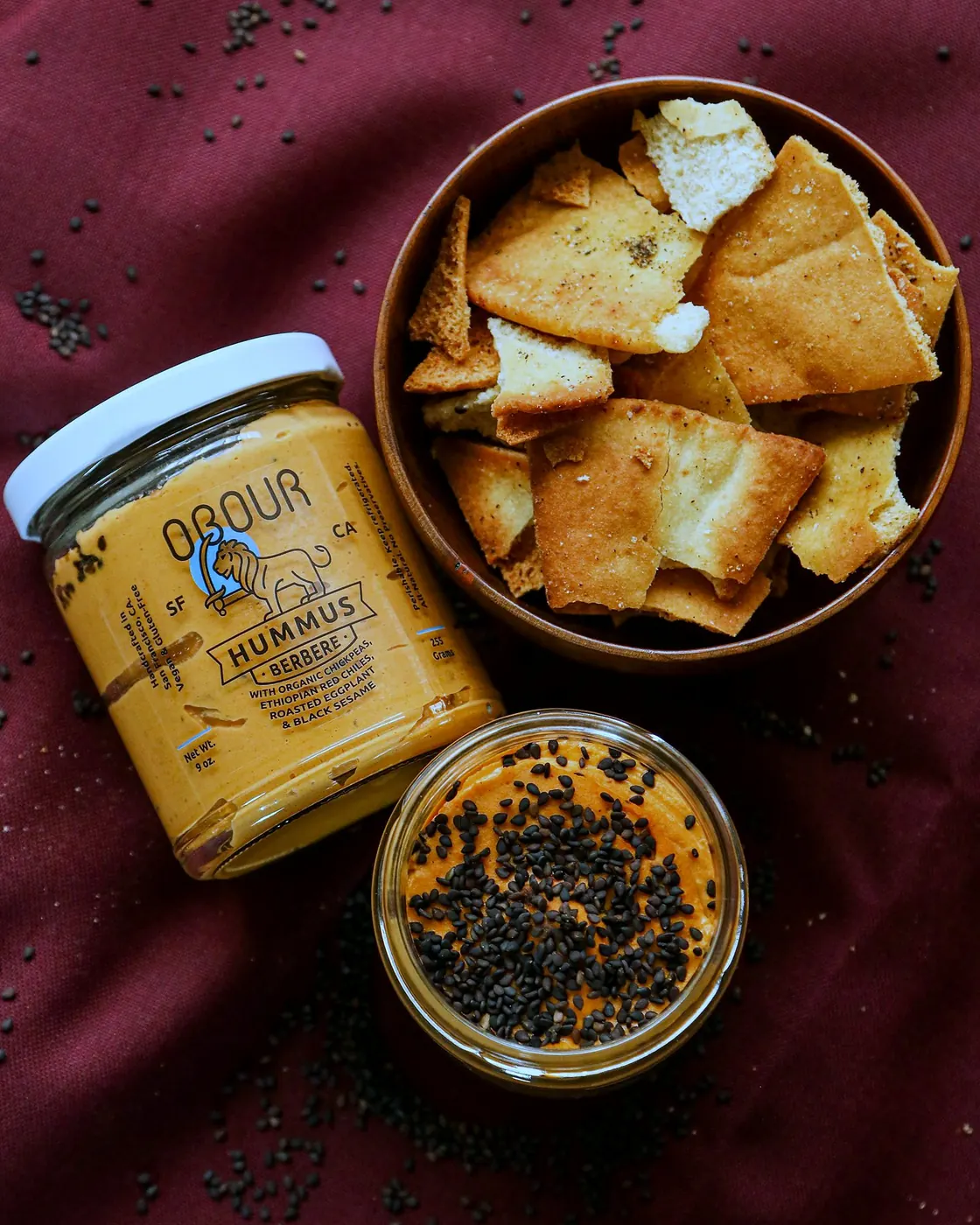 A bowl of pita chips next to jars of Berbere hummus
