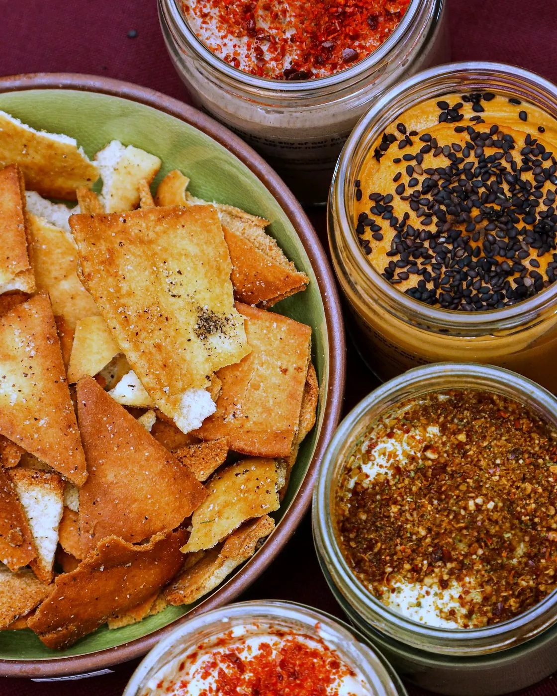 A bowl of Obour pita chips surrounded by open jars of hummus